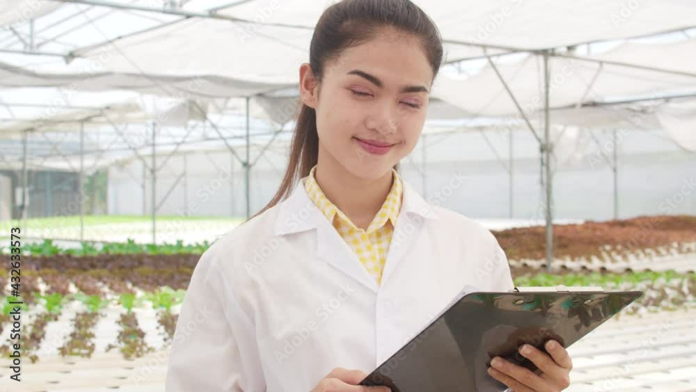 Close-up Happy Asian scientist woman looking at camera with smile hold document for research and development in organic vegetable at greenhouse farm garden, New technology in the cultivation concept. Close-up Happy Asian scientist woman looking at camera with smile hold document for research and development in organic vegetable at greenhouse farm garden, New technology in the cultivation concept.