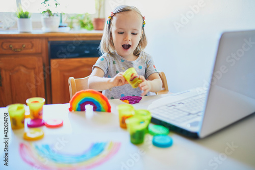 Toddler girl playing modelling clay in front of laptop