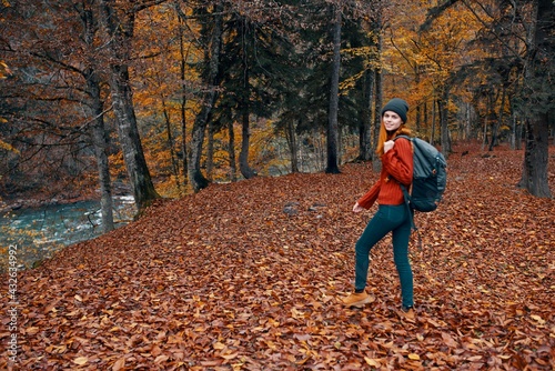 a full-length traveler with a backpack walks in the park with fallen leaves near the river