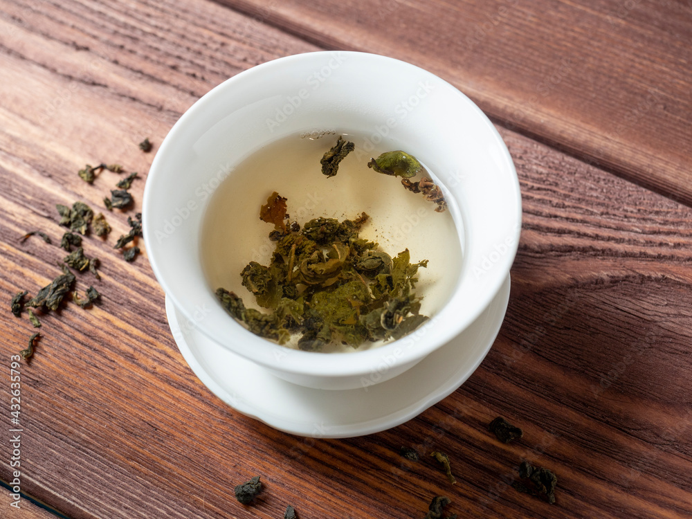 green tea is brewed in a white bowl on a wooden background. Dry tea leaves lie nearby. Top view green tea is brewed in a white bowl on a wooden background. Dry tea leaves lie nearby. Top view