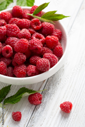Close up of red ripe raspberries in white bowl on wooden
