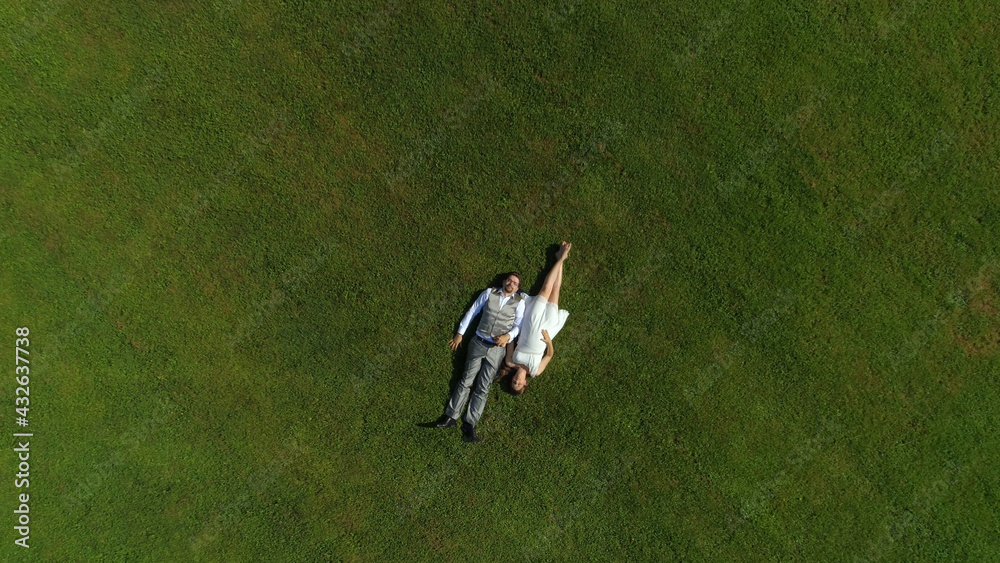 AERIAL TOP DOWN: Young excited parents to be lying down on grass on sunlit day AERIAL TOP DOWN: Young excited parents to be lying down on grass on sunlit day