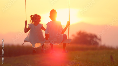 Obraz na płótnie LENSE FLARE: Couple young children swaying and holding hands at golden sunset