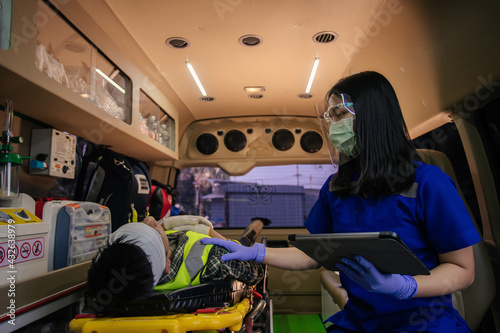 In epidemic crisis coronavirus (COVID-19), Asian female paramedic provide medical help to injured accident on ambulance in transfer patient. photo