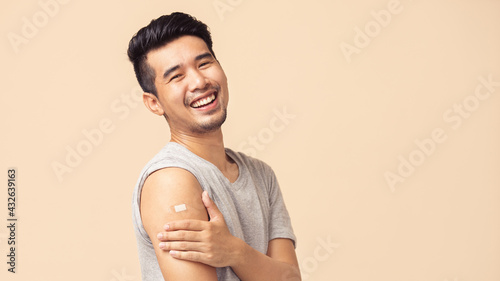 Portrait of Asian man showing his shoulder with bandage after getting a vaccination during covid-19 immunization program.