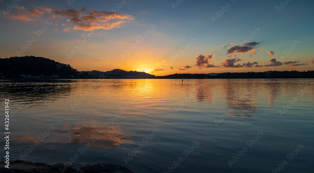 Sunrise panorama waterscape with scattered clouds and reflections