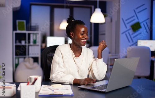 Happy african woman after reading email with good news working late at night. Enthusiastic winner employee using modern technology celebrate online win success reading great data.