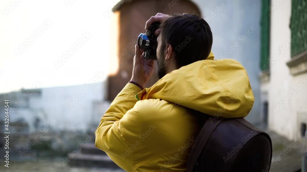 Adult male tourist photographer in yellow jacket taking photos with old film camera. Male backpacker with film camera traveling at the ancient city