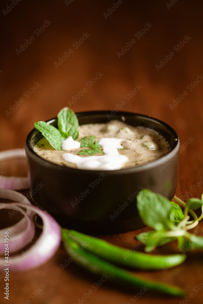 Close-up of Methi-Matar-Malai with white curry with fresh green chilies, mint leaves, and onions. A popular, delicious Indian recipe in a black bowl over wooden background. Close-up of Methi-Matar-Malai with white curry with fresh green chilies, mint leaves, and onions. A popular, delicious Indian recipe in a black bowl over wooden background.