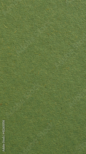 Green cardboard sheet. Eye-pleasing mobile phone wallpaper. Olive vertical background. Rough natural paper texture with cellulose fibers. Coloured paperboard of a calm and soft tint. Macro