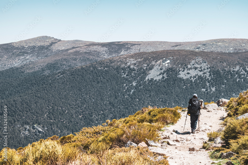 Hiker on his way to the top of a mountain with a great landscape on his left and copy space.