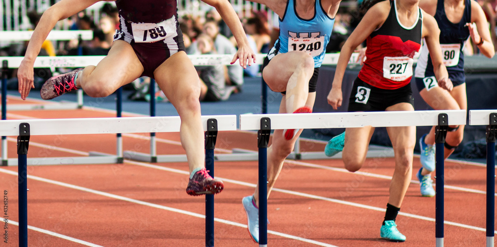 Fototapeta premium Four girls running in an indoor hurdle race