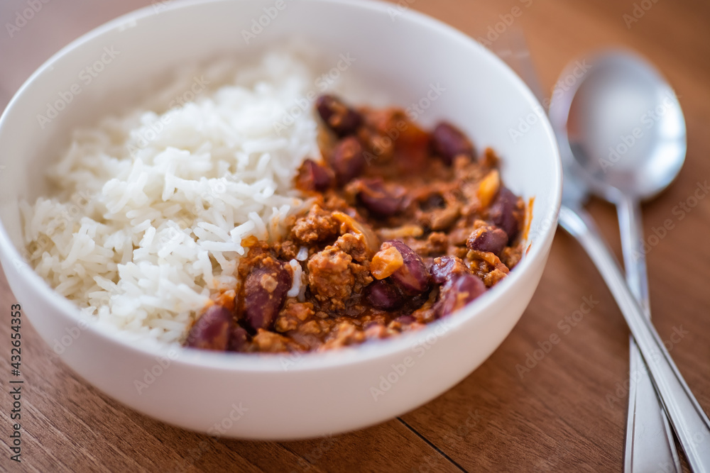 Close up and selective focus of meat chilli concarne and white rice in a white bowl on a wooden surface with intentional shallow depth of field and bokeh Close up and selective focus of meat chilli concarne and white rice in a white bowl on a wooden surface with intentional shallow depth of field and bokeh