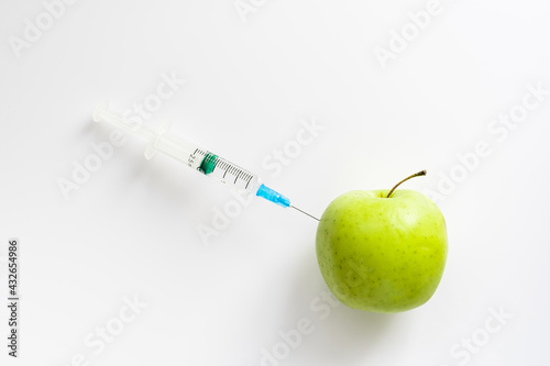 a laboratory assistant injects genetically modified substances into an apple with a syringe. experiments on crossing different varieties of fruits
