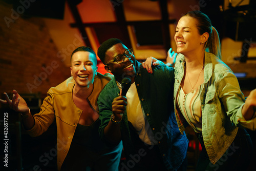 Cheerful African American man singing karaoke with female friends during a night out at the pub. photo