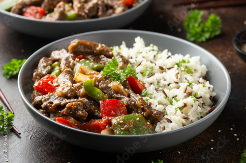 Stir fry Chinese pepper beef steak with onion, red and green bell pepper, rice in bowl