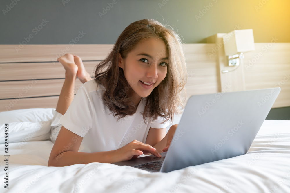Asian woman lying down and smiling the bed and laptop Asian woman lying down and smiling the bed and laptop