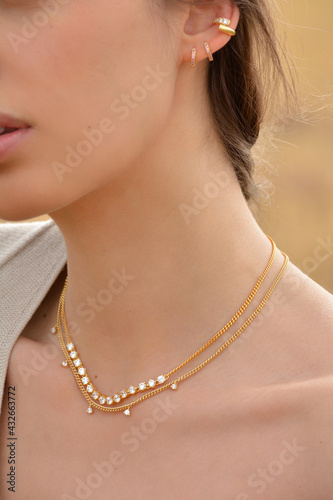 Close-up of a beautiful young blonde woman s neck  with gold earrings and pearl   gold and diamonds necklaces