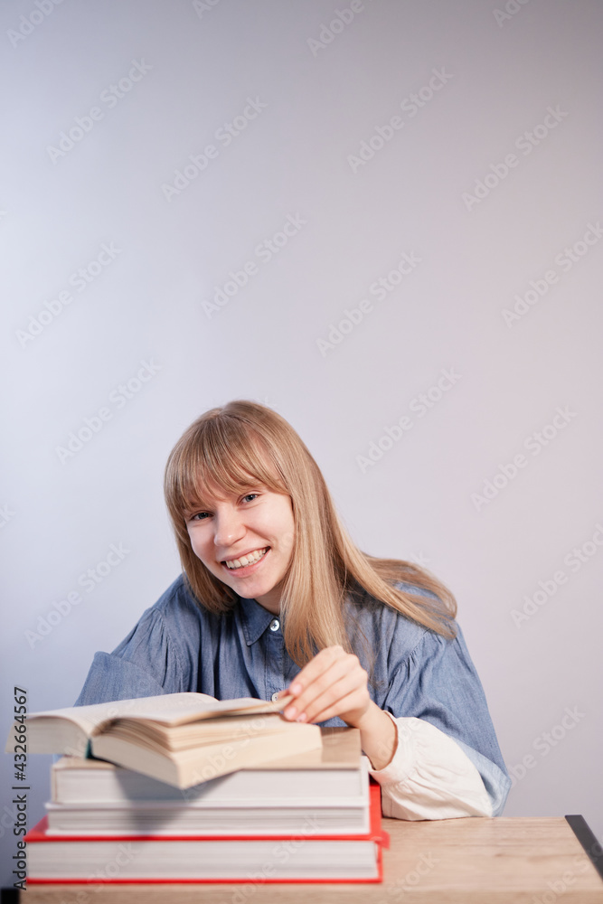 Homeschooling or back to school concept. Blonde female student with stack of books relaxing. Young beautiful caucasian pupil girl with opened book in class with copy space. High quality vertical photo Homeschooling or back to school concept. Blonde female student with stack of books relaxing. Young beautiful caucasian pupil girl with opened book in class with copy space. High quality vertical photo