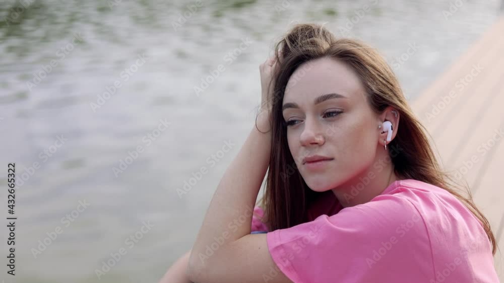 young girl with a smartphone in her hands is sitting on the shore of the lake and listening to music with headphones. video young girl with a smartphone in her hands is sitting on the shore of the lake and listening to music with headphones. video