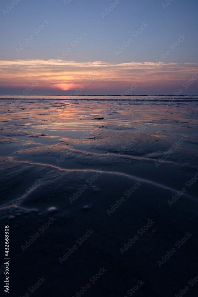 Ameland,Netherlands April 2021:Beach sunset, sunrise reflecting on wet sand. Cold blue and orange golden sunset over North sea coast.