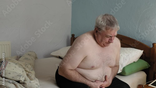 Obese white male with indegestion sitting on edge of bed in discomfort 1  photo