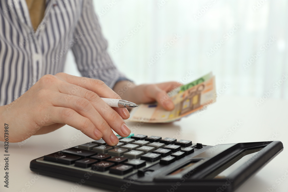 Woman counting money with calculator at table, closeup Woman counting money with calculator at table, closeup