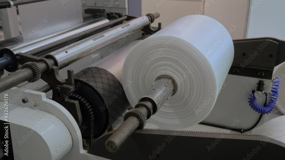 Moving roller with flat polyethylene transparent film - automatic plastic bag making machine at exhibition, trade show. Recycling, manufacturing, industry, automated technology equipment concept