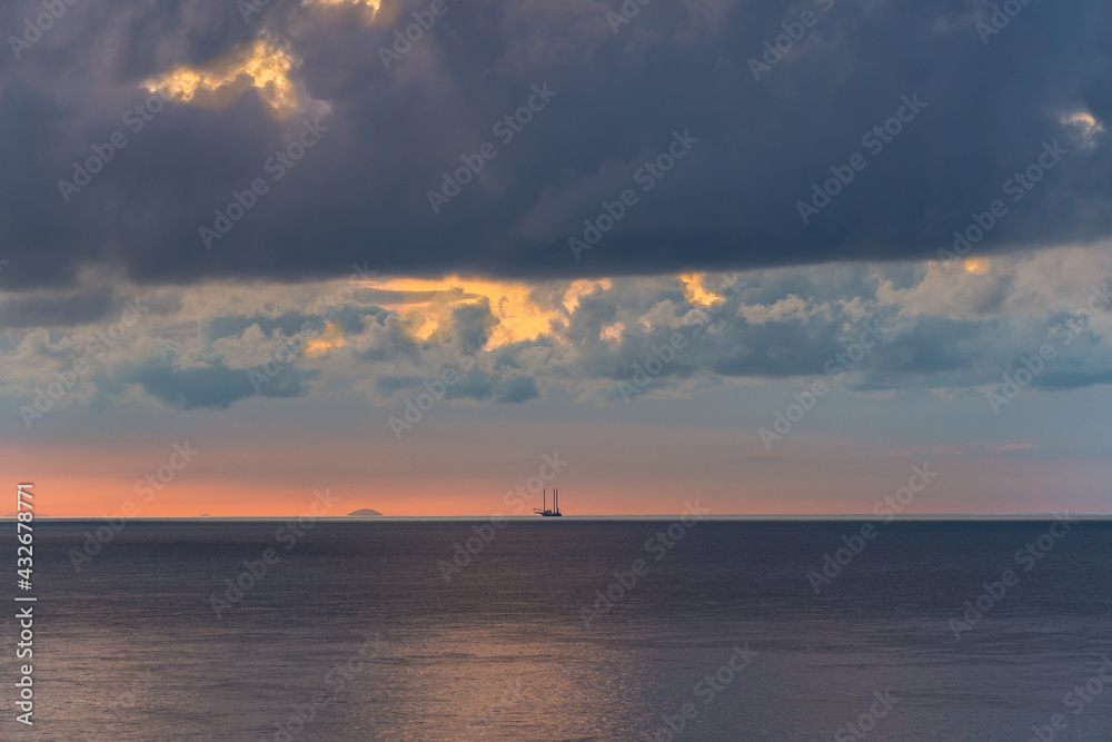 a small boat on the horizon at sunrise with incredible clouds