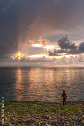 man in red jacket standing on cliffs watching sunrise over ocean in Greystones Ireland © Simon