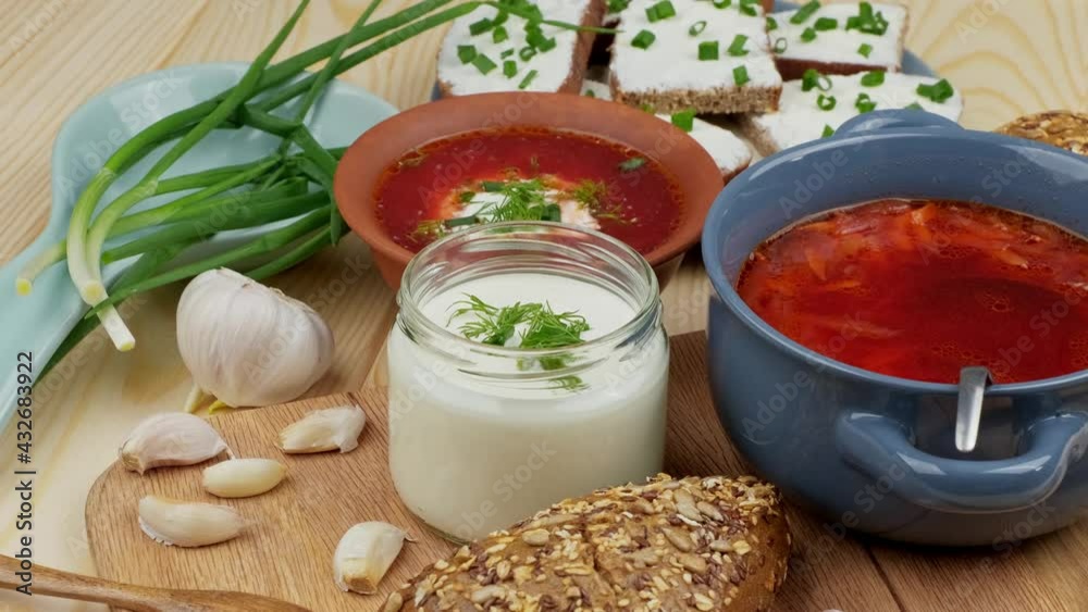 Russian and Ukrainian cuisine. Borscht with sour cream and spices, fresh herbs, garlic and pampushki. Beetroot soup in a blue bowl on a wooden board.