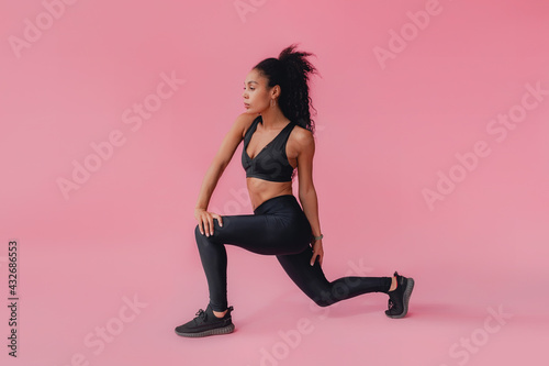 attractive black african american woman in black leggins fitness outfit on pink background © mary_markevich