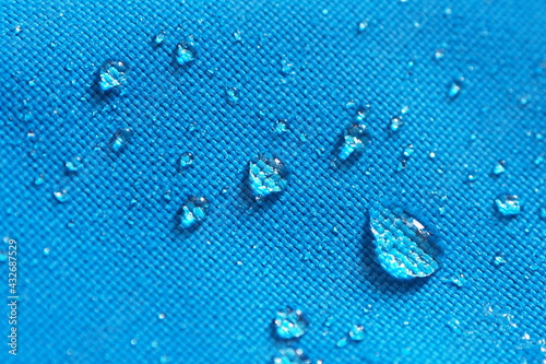 Closeup of water drops on bright blue fabric with waterproof design to protect fabric of the cloth from humidity and to offer easy cleaning to users Fabric texture with design and background concept photo