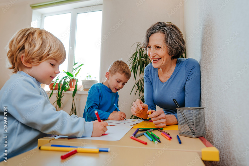 Fototapeta premium Grandmother drawing with her grandchildren sitting at the table