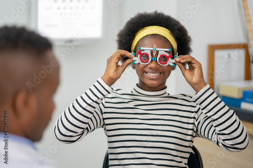 Happy Young black woman checking vision with eye test glasses during a medical examination at the ophthalmological office, ophthalmology concept. photo