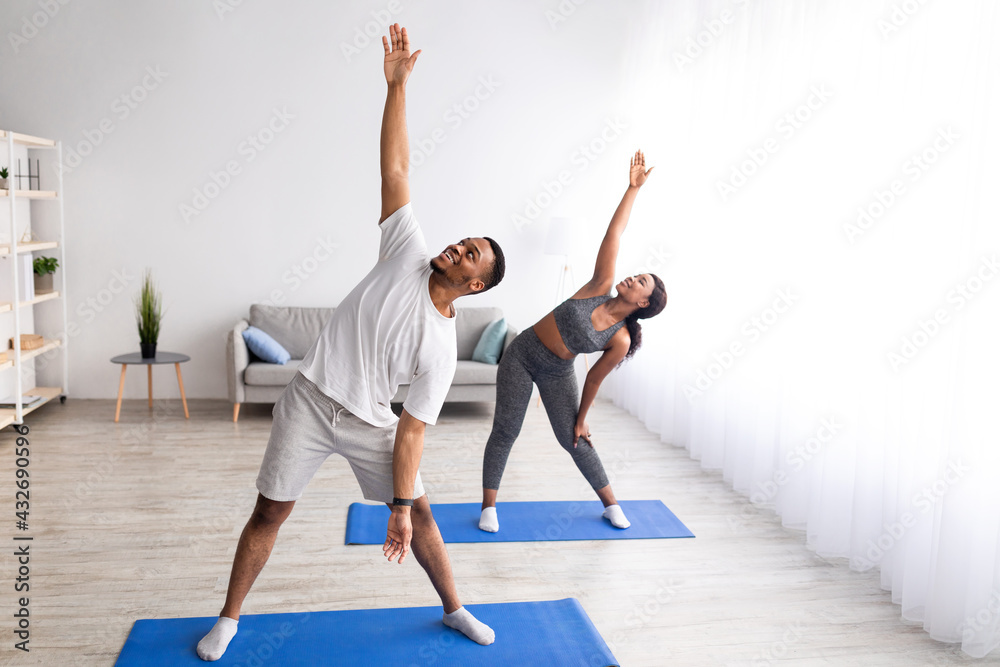 Young black couple practicing yoga at home, standing in triangle pose, copy space Young black couple practicing yoga at home, standing in triangle pose, copy space