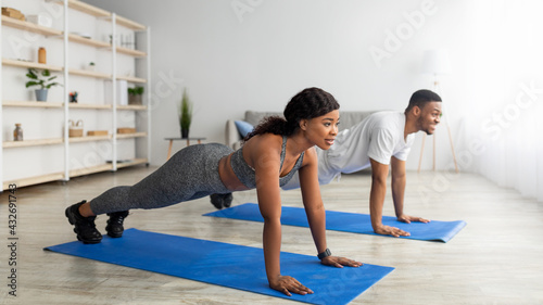 Millennial black couple standing in plank position on yoga mats at home, panorama