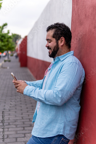 Young bearded mexican man wearing a blue dress shirt smiling as he looks at his smartphone in the magic town of Cholula, Mexico