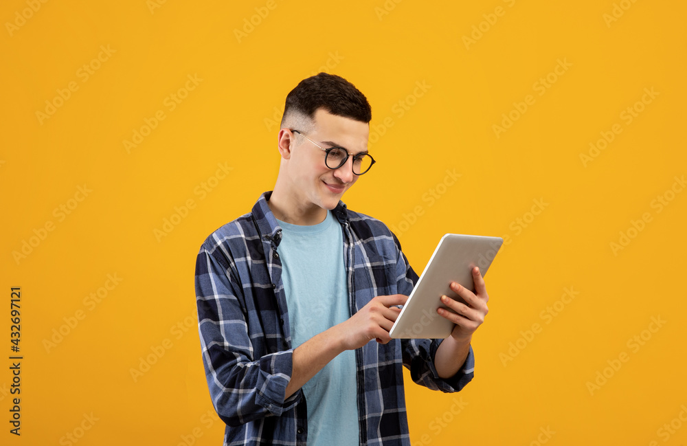 Online work, communiction, education. Cool young man browsing web on tablet pc over orange studio background Online work, communiction, education. Cool young man browsing web on tablet pc over orange studio background