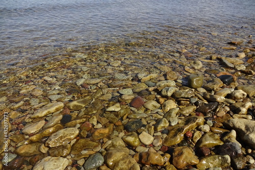 Yellow and brown colors pebble stones' backdrop on the beach in transparent water with a wave coming on a sunny day