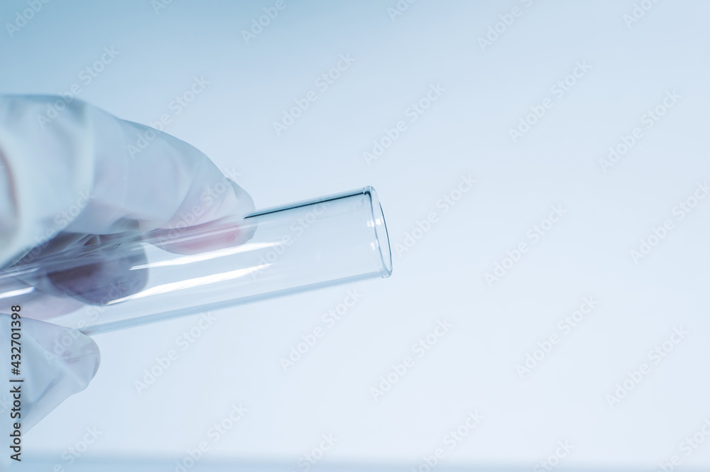 Medical laboratory. A gloved hand holds an empty test tube against a blue background. Medical laboratory. A gloved hand holds an empty test tube against a blue background.