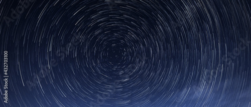 Obraz na płótnie Stellar trails, the rotation of bright stars at night around the Polar Star against a blue sky w salonie