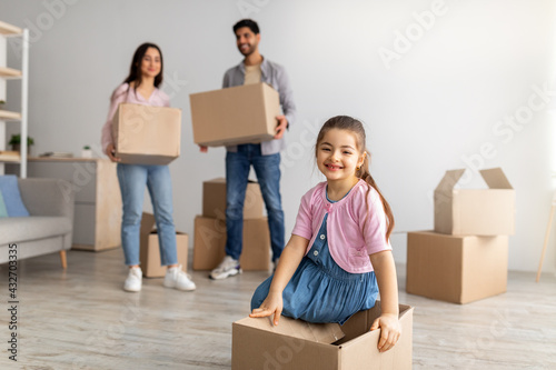 Relocation concept. Young eatern family with daughter moving house and unpacking boxes in new flat indoors photo