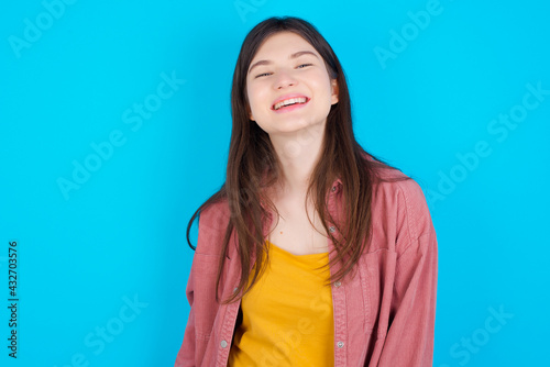 young beautiful Caucasian woman wearing pink T-shirt over blue wall with broad smile, shows white teeth, feeling confident rejoices having day off.