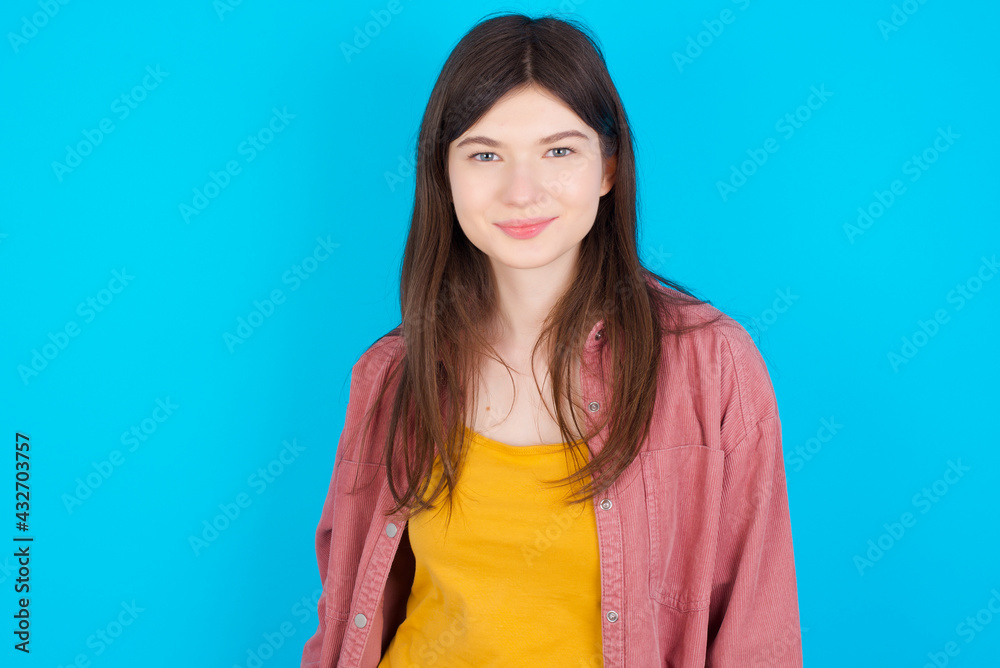 Happy young beautiful Caucasian woman wearing pink T-shirt over blue wall looking at camera with charming cute smile. Happy young beautiful Caucasian woman wearing pink T-shirt over blue wall looking at camera with charming cute smile.