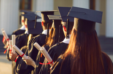 Rear view of university graduates crowd group line up holding degree certificate award in graduation ceremony. End of education and successful study and students congratulation concept