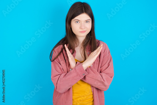 young beautiful Caucasian woman wearing pink jacket over blue wall Has rejection angry expression on face and crossing hands doing refusal negative sign.