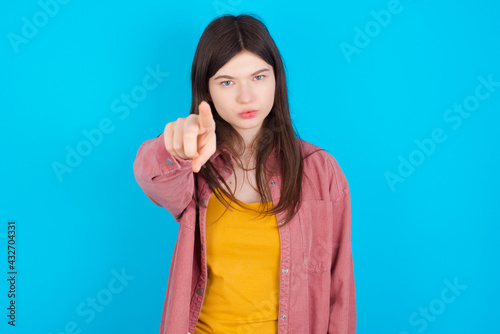 Cheerful young beautiful Caucasian woman wearing pink jacket over blue wall indicates happily at you, chooses to compete, has positive expression, makes choice.