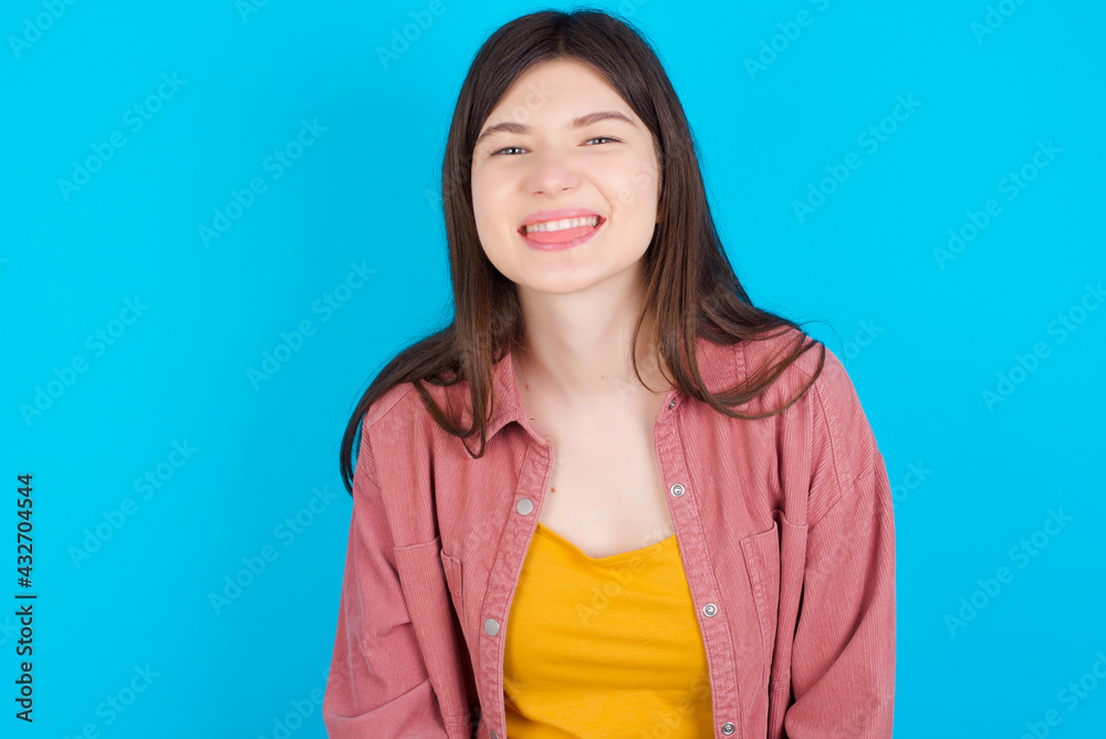Fototapeta premium young beautiful Caucasian woman wearing pink jacket over blue wall with happy and funny face smiling and showing tongue.