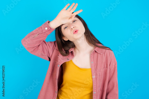 young beautiful Caucasian woman wearing pink jacket over blue wall wiping forehead with hand making phew gesture, expressing relief feels happy that he prevented huge disaster. It was close enough